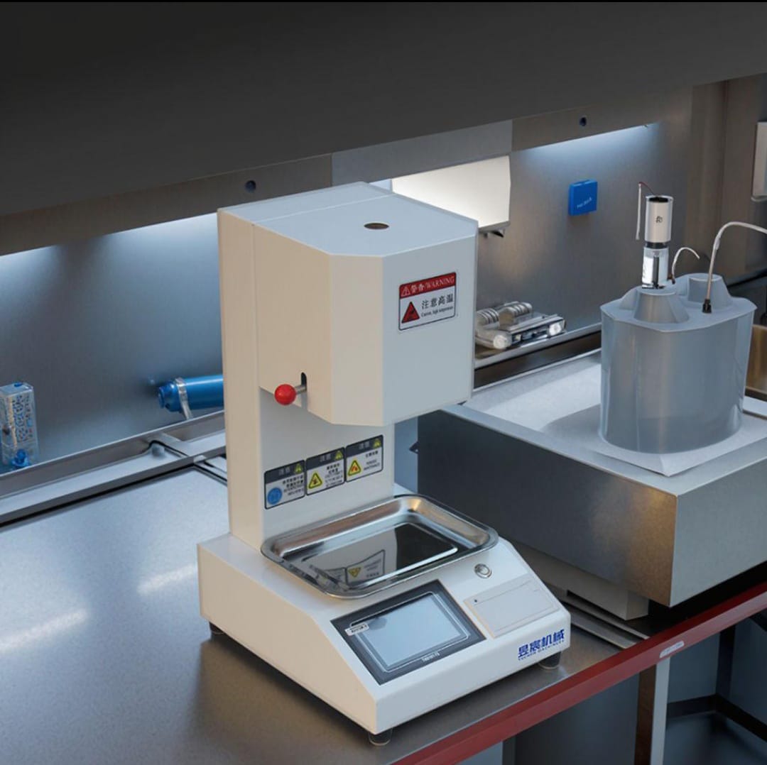A laboratory grade melt flow indexer installed on a bench alongside auxiliary sample preparation equipment.